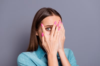 Woman with hands in front of face peaking out between fingers looking embarrassed about pregnancy incontinence