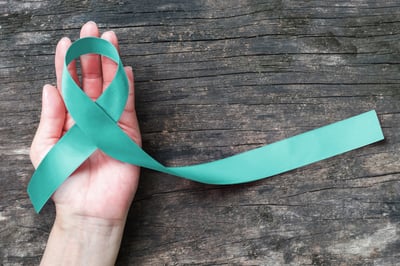 Teal PCOS awareness ribbon in woman's hand on a distressed piece of wood background
