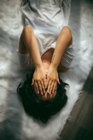 Woman laying on bed with her hands covering her face from painful emotional and physical symptoms of polycystic ovarian syndrome