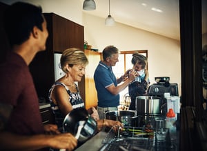 new parents to a newborn baby with their parents in the kitchen. New mom holding baby as grandma and new dad help with dishes