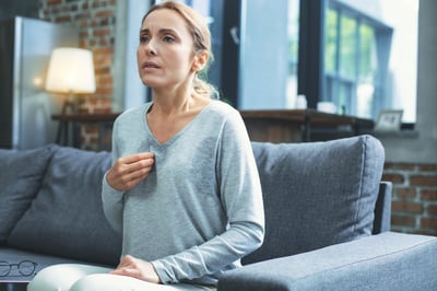 Mature woman sitting on couch experiencing menopausal symptoms like sweating and hot flashes