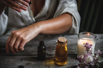 pregnant woman using safe essential oils sitting at table using a dropper to pour oil on arm