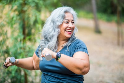 A middle-aged woman smiling and walking on a trail with weights in her hands as she exercises to reverse or prevent osteoporosis