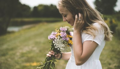 a girl in a grassy field smelling a bouquet of wild flowers