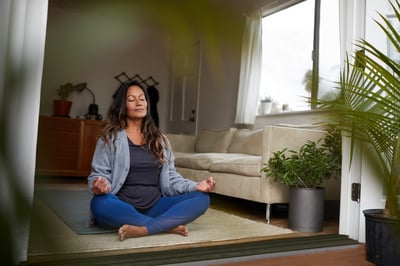 a mature woman experiencing menopause in a dimply-lit room and relaxing atomosphere practicing yoga for menopause symtpoms