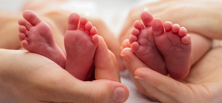 Mother and fathers hands cradling twin babies feet