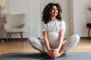 Pregnant woman with curly hair practicing yoga in a bright room