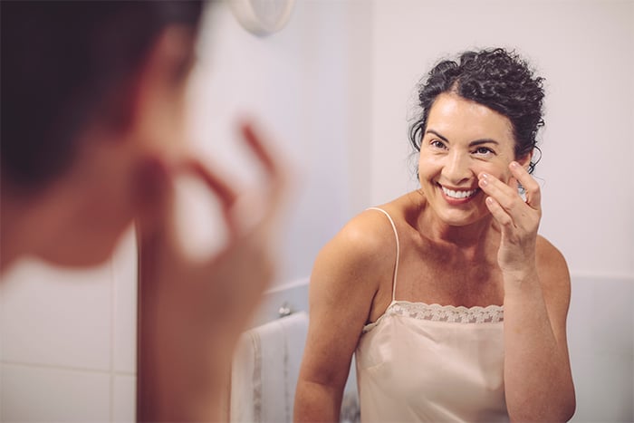 happy woman inspecting her skin at home